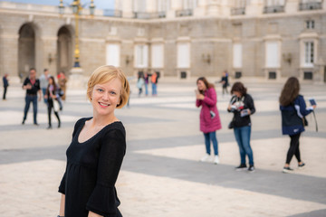 A woman enjoys traveling in Spain and poses for photos in the beautiful Plaza de la Armería in front of the Royal Palace. Photography is permitted outside the palace.