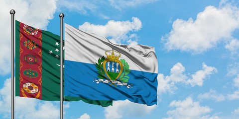 Turkmenistan and San Marino flag waving in the wind against white cloudy blue sky together. Diplomacy concept, international relations.