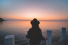 One Lonely Carefree Traveler Woman In A Hat On A Sea Pier At Sunset. Happy Concept, Free People And Enjoying Life