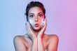 Portrait of beautiful woman looking at camera with surprising. Wonderful young lady washing face with cleansing skin foam. Beauty and cosmetics concept. Bright neon background
