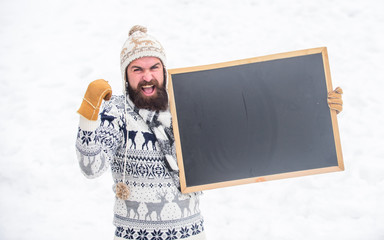 Poster - Emotional guy snowy nature background. Winter announcement. Hipster knitted hat and gloves show blackboard. Winter event. Man with beard hold chalkboard copy space. Check it out. Winter holidays