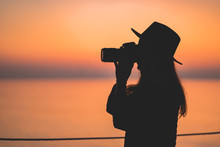Silhouette Of A Woman Photographer In Hat With Dslr Camera During Taking Photos At Sunset