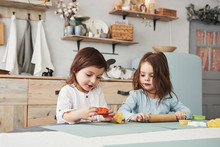 Just Having Free Time. Two Kids Playing With Yellow And Orange Toys In The White Kitchen
