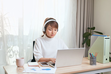 Fototapete - Young Asian businesswoman listening to music and working with laptop at home