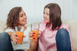 © Andrii - Blurred afro-american and caucasian girl friends holding glasses of fresh juice in front of the camera, looking at one another, smiling.