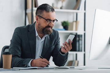 Wall Mural - handsome businessman in formal wear holding smartphone and pen