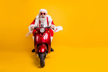 Full length photo of crazy funky santa claus in red hat drive motorcycle ride fast hurry to x-mas noel celebration wear shirt suspenders isolated over yellow color background