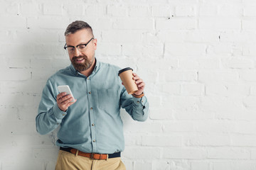 Wall Mural - handsome businessman in shirt and glasses holding smartphone and paper cup