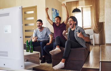 Celebrating victory. Excited three friends watching soccer on TV at home together