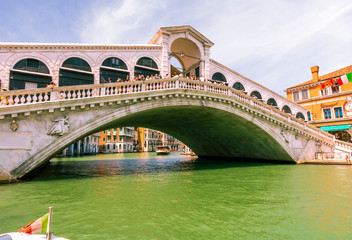 picturesque view at Rialto bridge in Venice with italian and venetian flags , tourists, old buildings and beautiful sky on background , water landscape