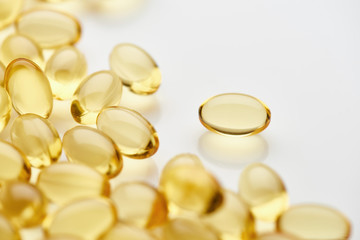 close up view of golden fish oil capsules scattered on white background