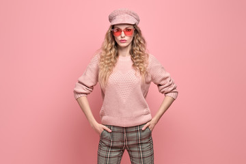 Fashionable woman in Trendy pink outfit, stylish hairstyle, makeup. Young blonde in jumper, cap. Sensual beautiful model girl in stylish sunglasses, pastel fashion beauty concept on pink