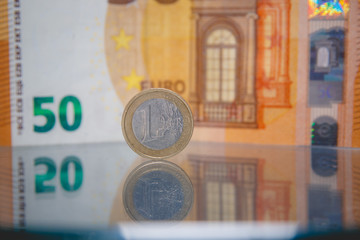 Macro photo of a coin in 1 euro on a blurred background banknote in 50 euro. Reflection of the coin on the glass table. Very small depth of field.