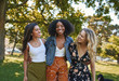 © StratfordProductions - Portrait of a group of happy three diverse young women hugging laughing and having fun in the park on a sunny day while walking
