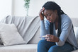 Depressed black girl holding pregnancy test, upset with positive result