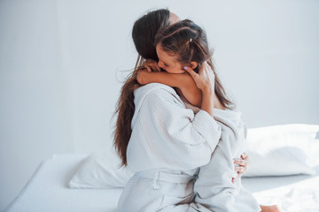 Wall Mural - Embracing each other. Young mother with her daugher have beauty day indoors in white room