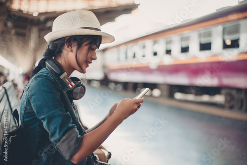 Asian tourist teenage girl at train station using smartphone map, social media check-in, or buy ticket booking. Modern travel app technology, lone traveler, Summer vacation railroad adventure concept