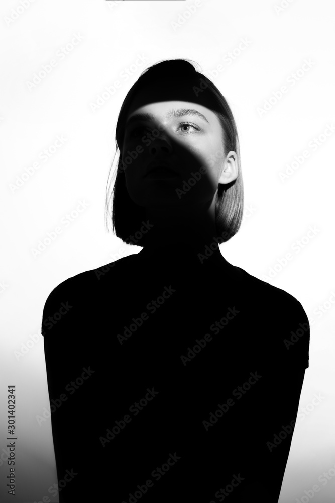 Fashionable beauty portrait. Black silhouette on white background. Girl with a spot of light on her face.  - obrazy, fototapety, plakaty 