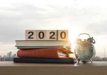 Wooden Blocks With The Word 2020, Notebook, Books And Clock On Table With Panoramic City Skyline Background In The Morning. Happy New Year, Start Up, Refresh, Mindset Concept.
