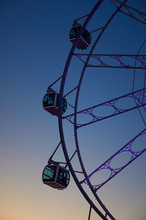 Ferris Wheel With Transparent And Public Booths Inside At Sunset In Yellow And Blue Gradient With The Lights On