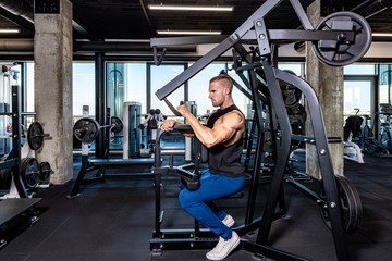 Young sweaty strong muscular fit man back muscles workout training with weights on the machine in the gym