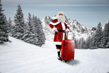 Wall Mural - Saint Nicholas with a red suitcase. Elderly man with a beard delivers presents to children. Christmas magic time. Winter landscape with mountain views and snowy trees. Fir branches covered with frost.