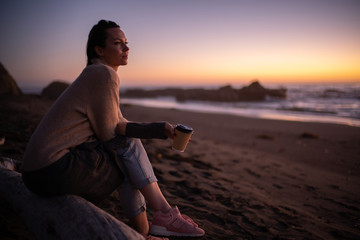 Woman enjoying hot drink on a sunset near ocean