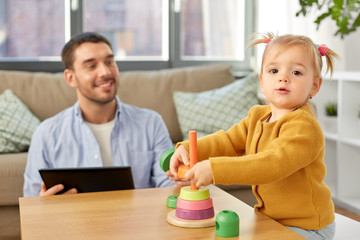 Canvas Print - family, fatherhood and people concept - happy father with tablet pc computer and little baby daughter playing with pyramid toy at home