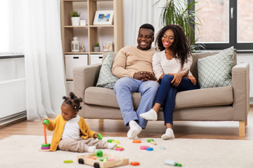 family, parenthood and people concept - happy african american mother and father looking at baby daughter playing with toy blocks at home