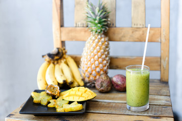 Nice bananas, carambola with pine apple and mango on wooden chair, green fresh kiwi juice.