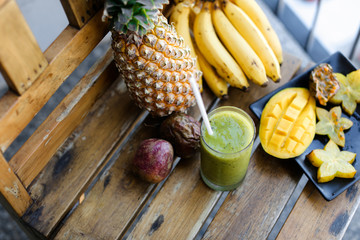 Big pine apple with bananas, carambola and mango standing on wooden chair, kiwi fresh juice.