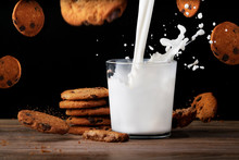 Glass Of Milk With Cookies. Milk Splashes. Flying Cookies. Close Up View On Black Background.