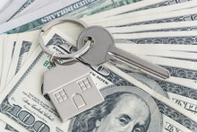 Home Keys And A Small House On Currencies Dollar Background. The Concept Of Renting Or Selling A House Or Flat, Mortgage, Investment Or Real Estate, Property Buying. Money For The Housing Plan