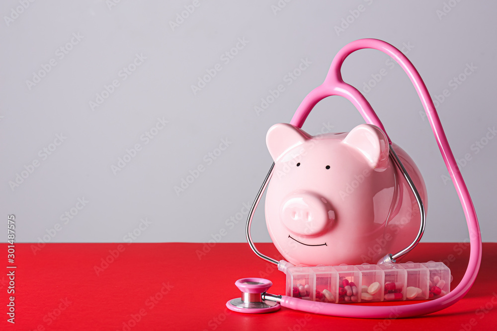 Piggy bank with stethoscope and pills on grey background