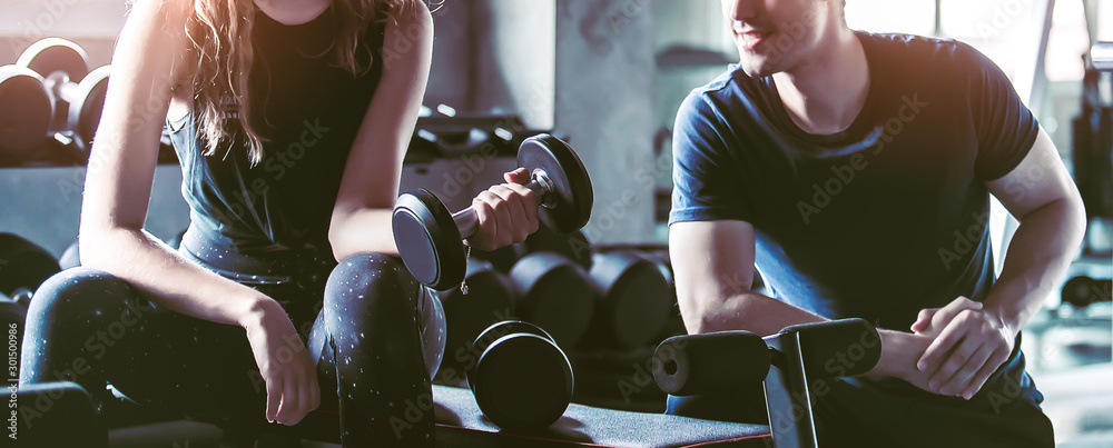 Crop image of beautiful sport girl with dumbbell in hand with personal trainer in professional gym, color filter effect selective focus. - obrazy, fototapety, plakaty 