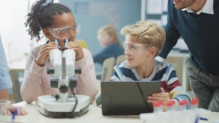 Poster - Elementary School Science Classroom: Cute Little Girl Looks Under Microscope, Boy Uses Digital Tablet Computer to Check Information on the Internet, while Enthusiastic Teacher Explains Lesson