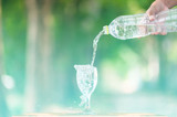 Fototapeta Łazienka - Water splash in glass Select focus blurred background.Drink water pouring in to glass over sunlight and natural green background.Nature conservation concept.