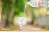 Fototapeta Łazienka - Water splash in glass Select focus blurred background.Drink water pouring in to glass over sunlight and natural green background.Nature conservation concept.