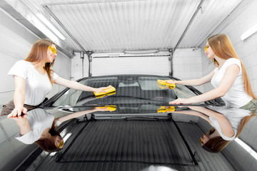 Two beautiful women worker washing windshield with sponge on car wash, window polishing