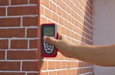 Hand held red laser distance meter Brown brick wall background Diagonal lines Sunlight Construction of house with masonry