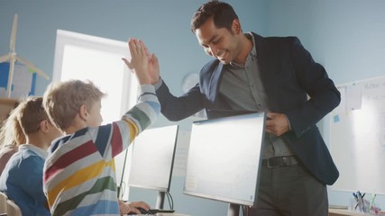 Elementary School Computer Science Classroom: Teacher Uses Tablet Computer, Explains Lesson to Diverse Group of Smart Children, Gives High Five to a Boy. Informatics Class for Children