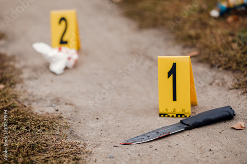 Fotografía Crime scene investigation, bloody knife with crime markers on the ground, eviden