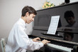 Young man enjoying playing an old nostalgic melody as he sits at an upright piano reading an old music score