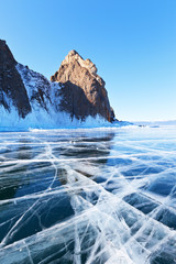 Winter landscape of frozen Baikal Lake. Famous Cape Khoboy - natural landmark of the Olkhon Island. A group of tourists at a cliff in the distance. Beautiful winter background