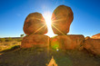 Australia, Northern Territory. Aboriginal land in Red Centre. Sunbeams sky at sunrise behind iconic the Eggs of mythical Rainbow Serpent at Karlu Karlu - Devils Marbles Conservation Reserve.