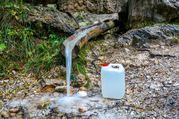 Filling fresh water from a mountain stream in a white plastic can for transport