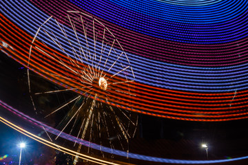 Wall Mural - Two rides in motion in amusement park, night illumination. Long exposure.