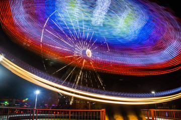 Wall Mural - Two rides in motion in amusement park, night illumination. Long exposure.