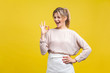© khosrork - Portrait of satisfied beautiful young woman with blonde hair in casual beige blouse standing, looking at camera showing Ok sign gesture and winking, indoor studio shot isolated on yellow background