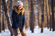 Portrait of young beautiful girl with long hair, in a blue jacket and knitted hat and mittens posing in sunny winter day. Fashion young woman in the winter forest. Christmas, winter holidays concept. 